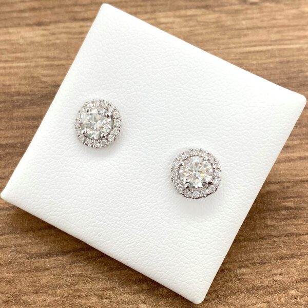 Diamond halo stud earrings on white display.