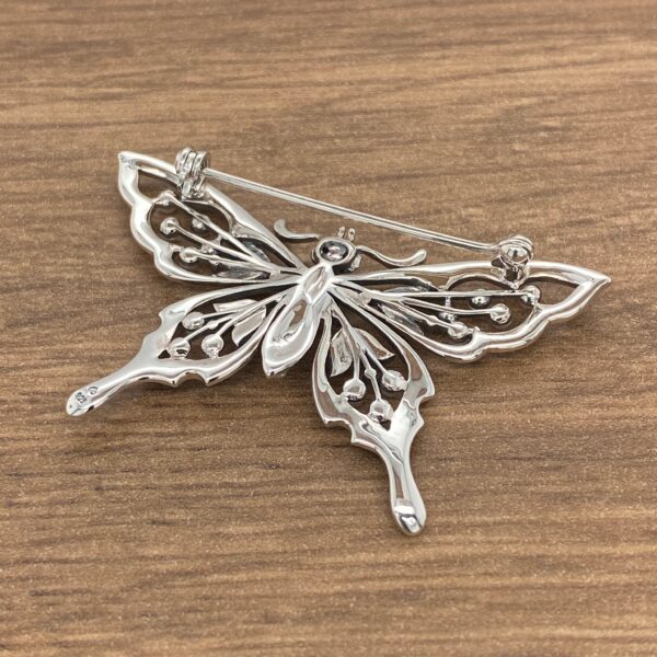 A silver butterfly brooch on top of a wooden table.