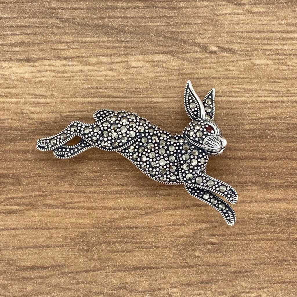 A silver rabbit brooch on top of a wooden surface.