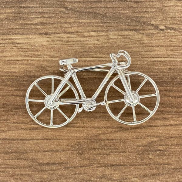 Silver bicycle brooch on wood grain background.