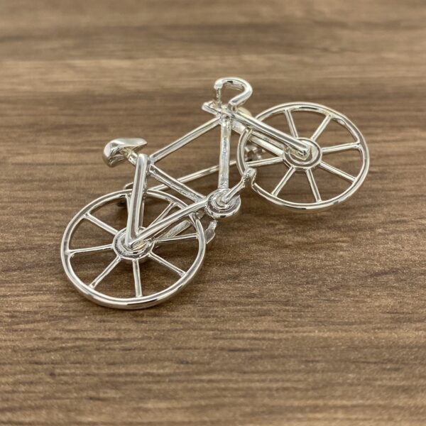 Silver bicycle brooch on wooden background.