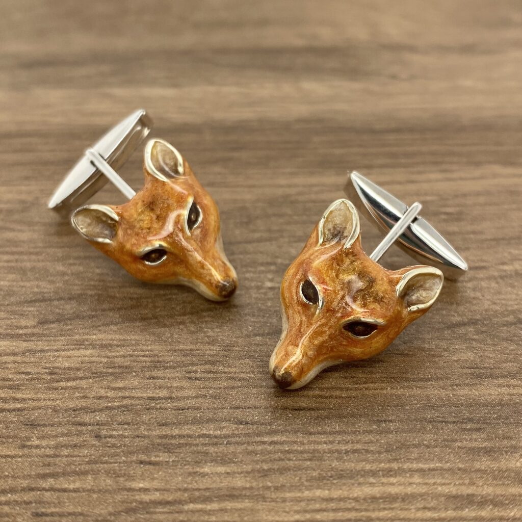 Two fox head cufflinks on a wooden table.