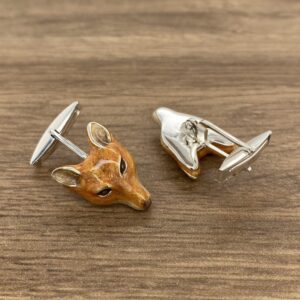 Two fox head cufflinks on a wooden table.
