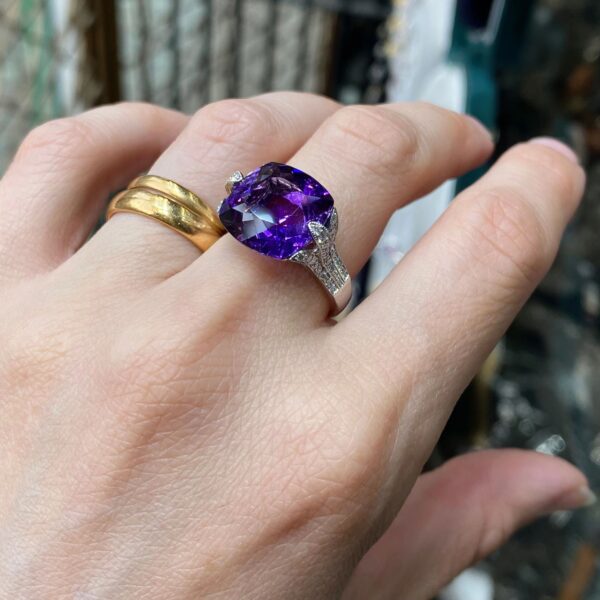 Amethyst ring with diamond accents on a hand.