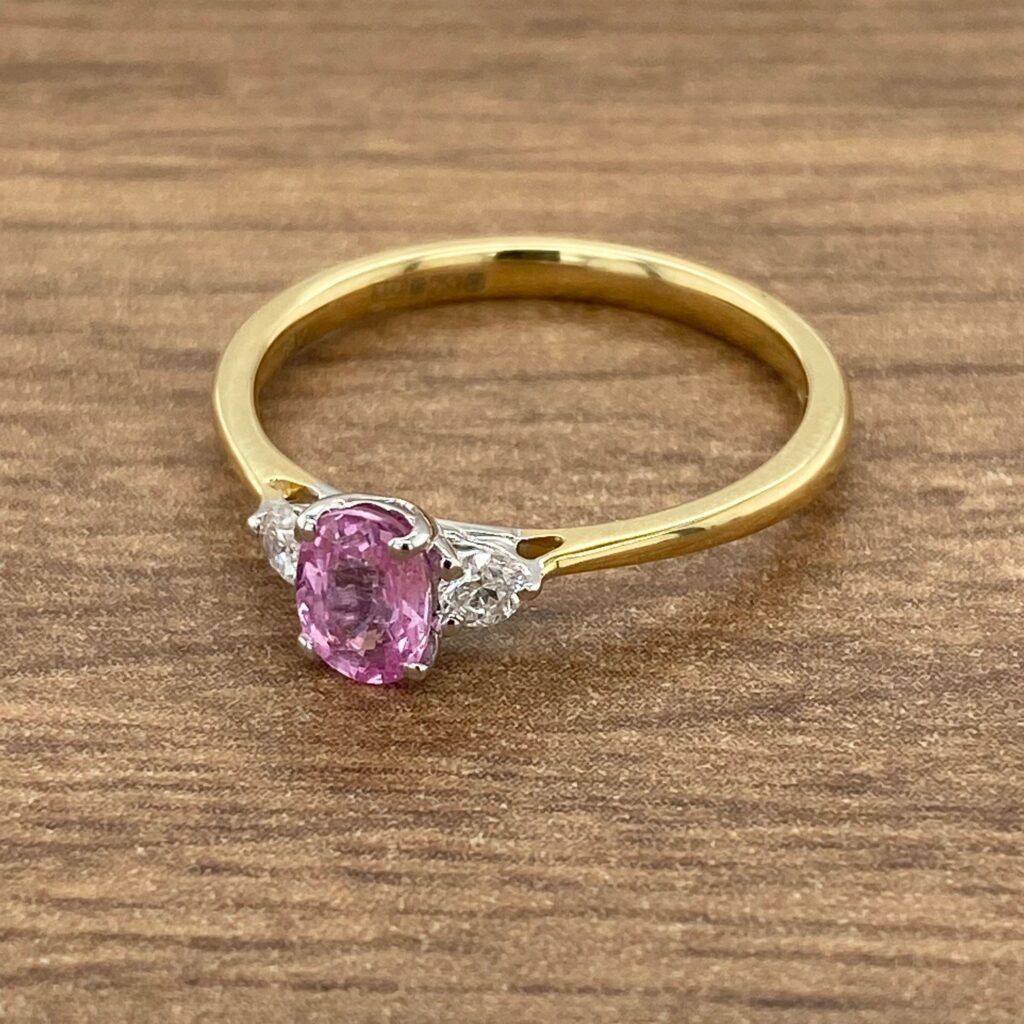 Pink sapphire and diamond ring on wood.