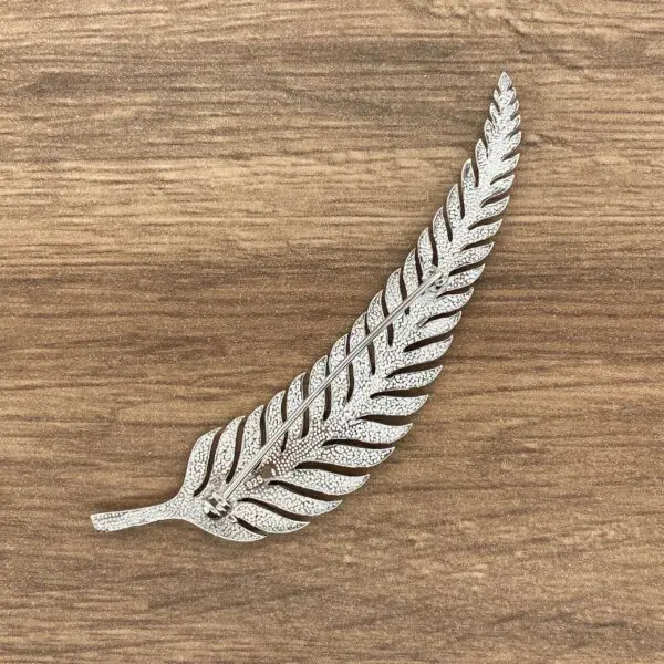 Silver fern leaf brooch on wood background.