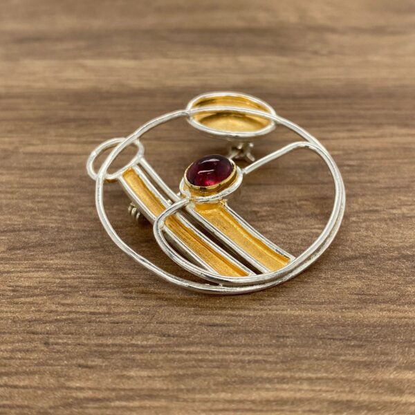 Silver and gold brooch with red gem.