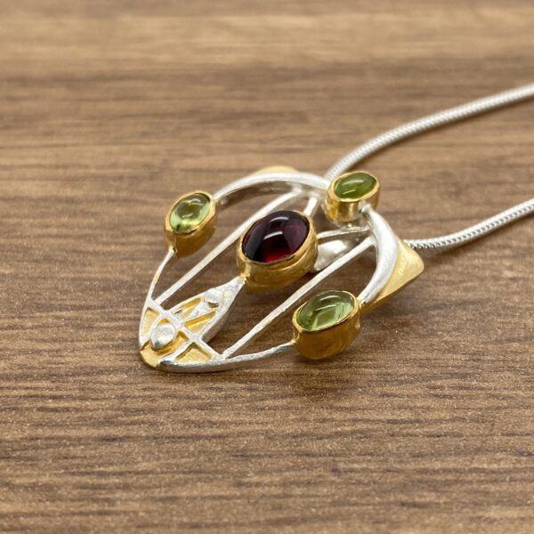 Silver and gold pendant with red and green stones.