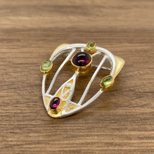 Silver and gold brooch with green and purple stones.