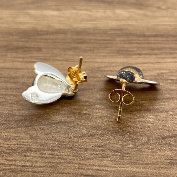 Two silver butterfly earrings with gold backs.