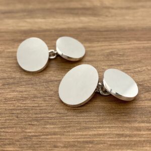 Two silver cufflinks on a wooden table.