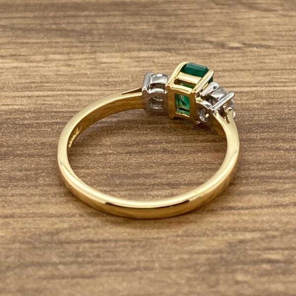 Emerald and diamond gold ring on wood.