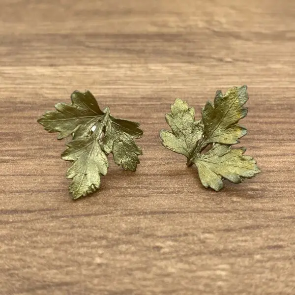 Gold leaf earrings on wooden background.