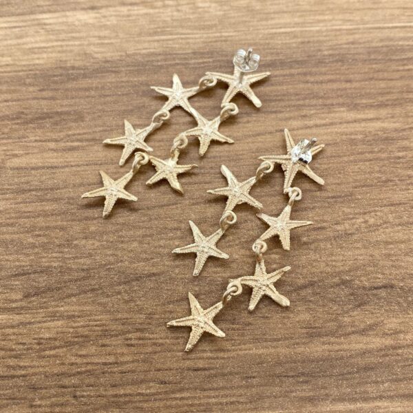 Gold starfish dangle earrings on wood.