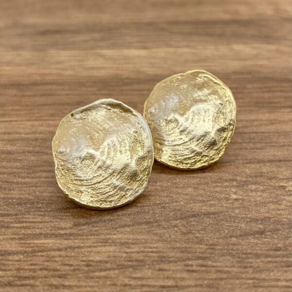 Gold textured round earrings on wood.