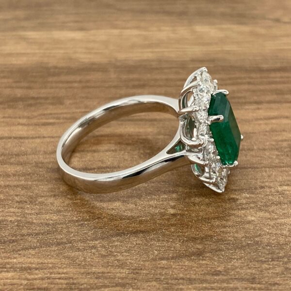 Emerald and diamond halo ring on wood.