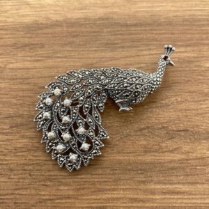 A silver peacock brooch with pearls.