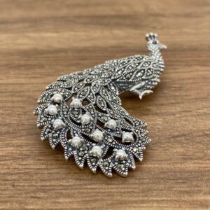A silver peacock brooch with pearls.