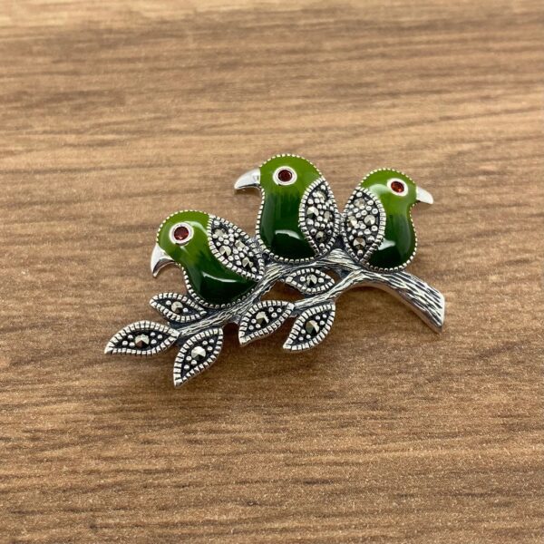 Silver brooch with three green birds on a branch.