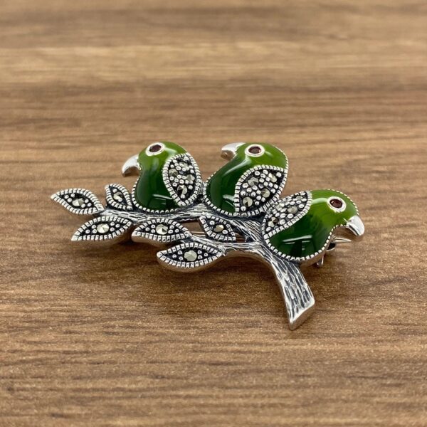 Silver brooch with three green birds.