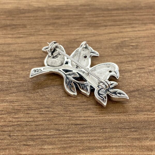 Silver bird brooch with leaves on wood.