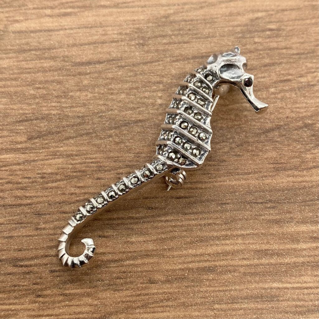 A silver seahorse brooch on a wooden table.