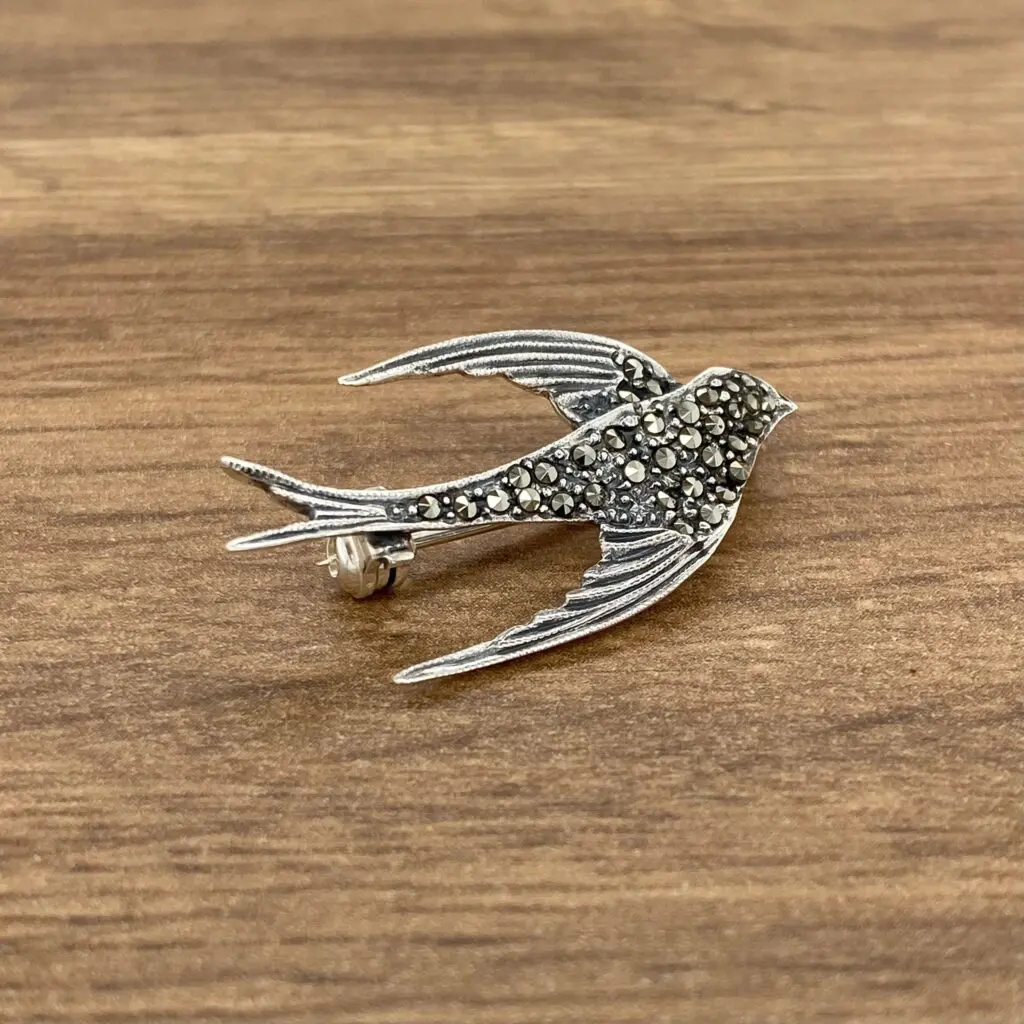 A silver bird brooch on a wooden table.