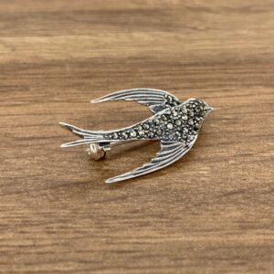 A silver bird brooch on a wooden table.