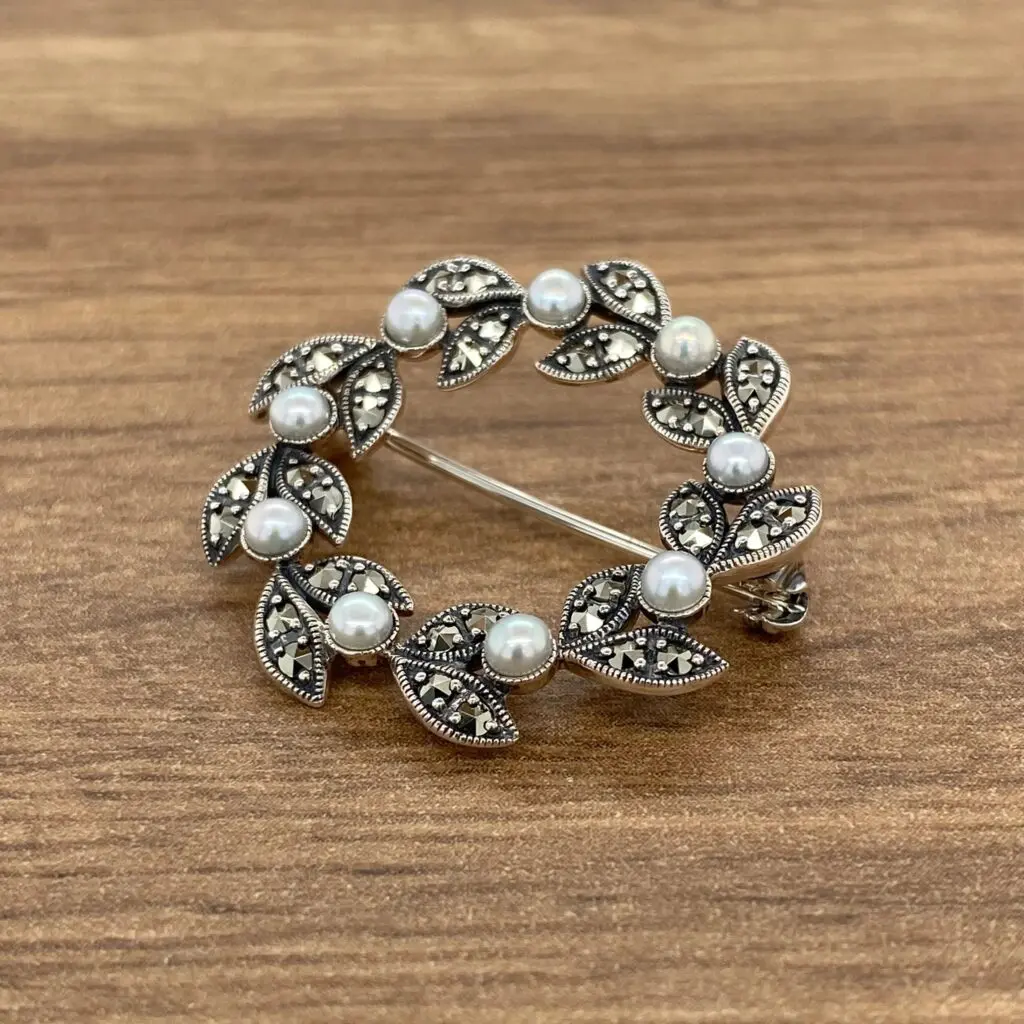 A brooch with pearls and leaves on a wooden table.