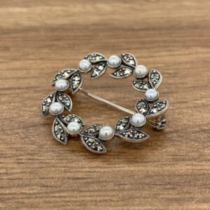 A brooch with pearls and leaves on a wooden table.