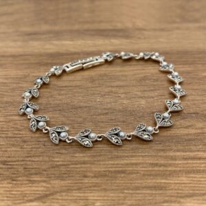 A silver bracelet with leaves and pearls on a wooden table.