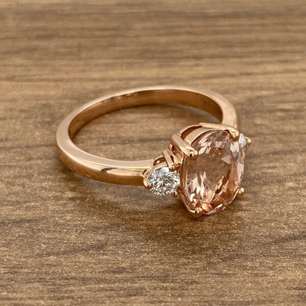 Rose gold ring with a pink gemstone and two diamonds.