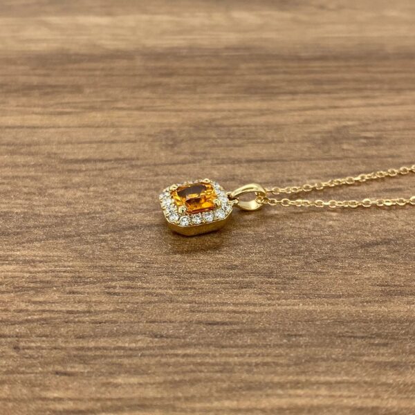 Gold necklace with a diamond and orange stone pendant.