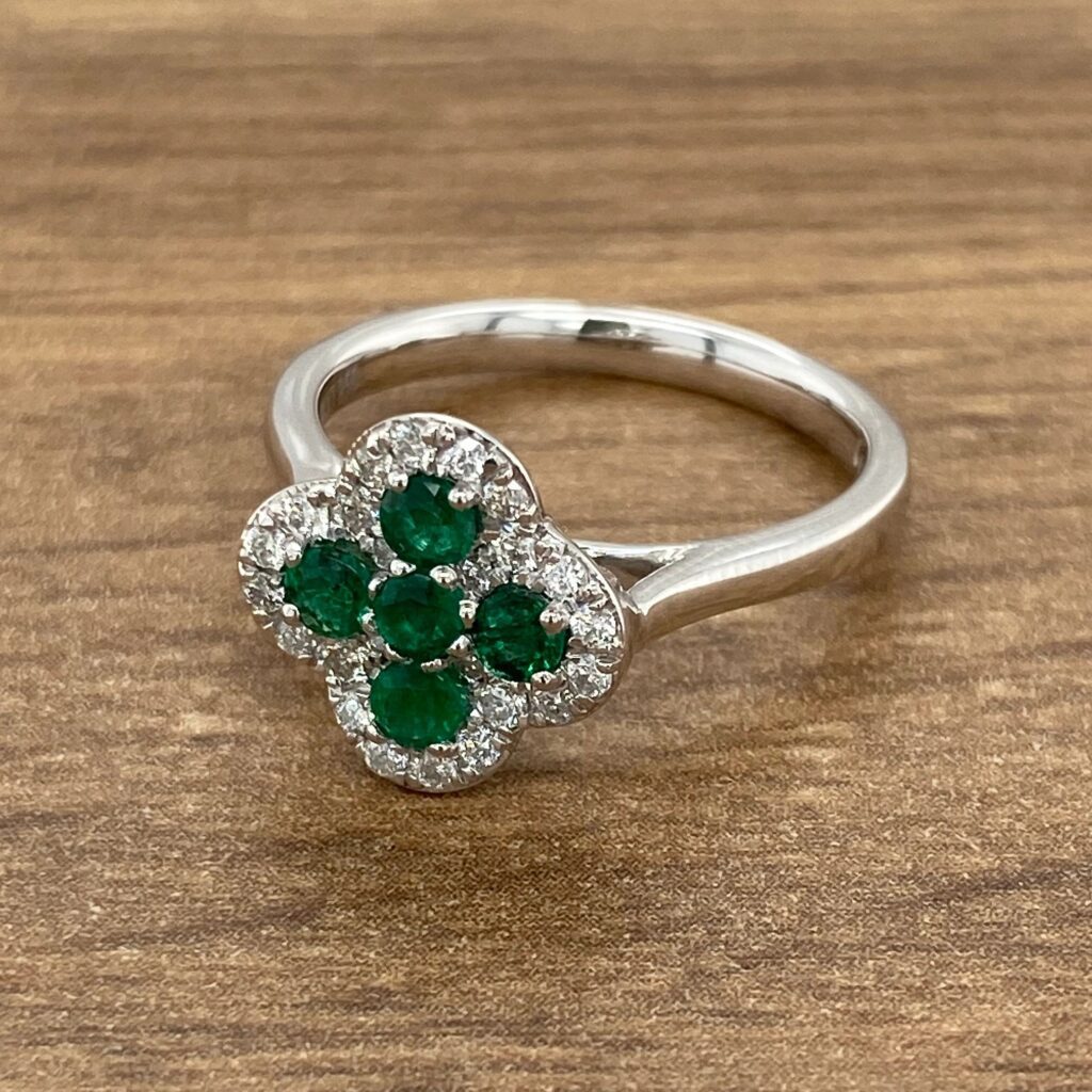 Emerald and diamond clover ring on wood.