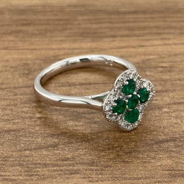 Emerald and diamond clover ring on wood.