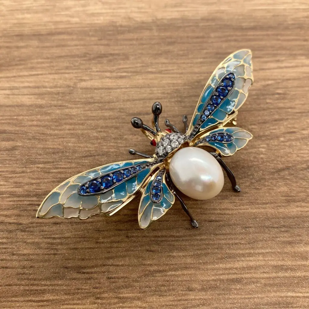 A brooch with a blue and white bee and pearls.