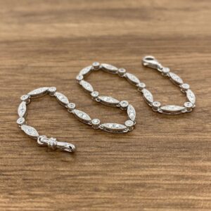 A silver bracelet with diamonds on it with a wooden background.