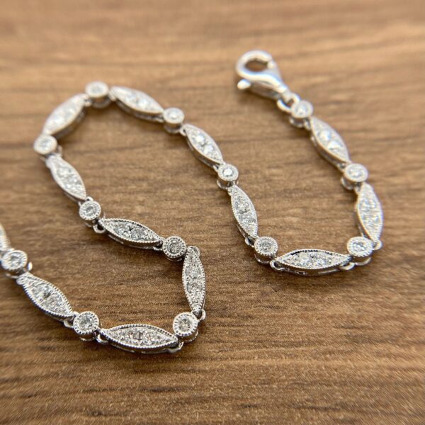 A silver bracelet with diamonds on it with a wooden background.
