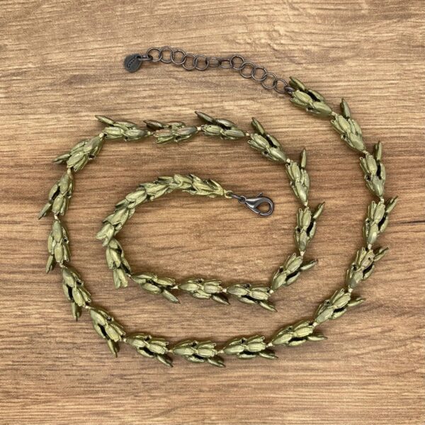 Green leaf-shaped metal necklace on wood.