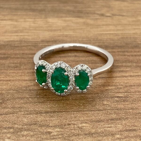 Three stone emerald and diamond ring on a wooden table.