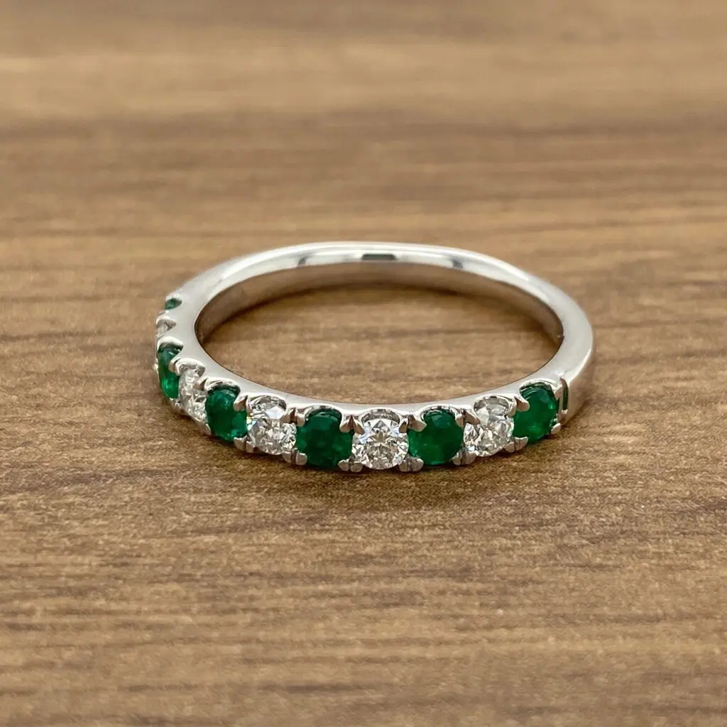 An emerald and diamond ring on a wooden table.