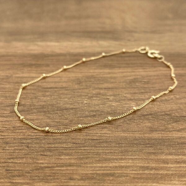 A gold beaded bracelet on a wooden table.