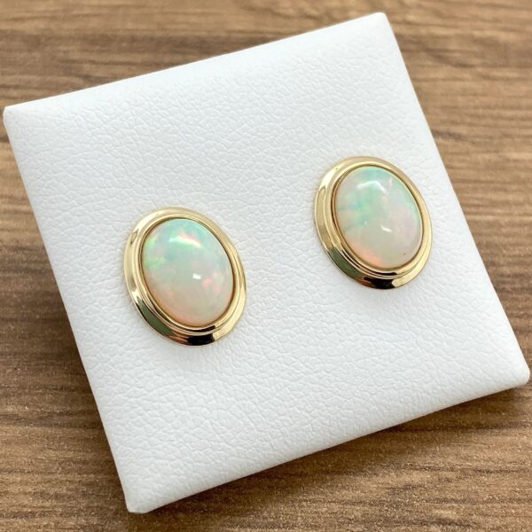 Gold opal earrings on white display.