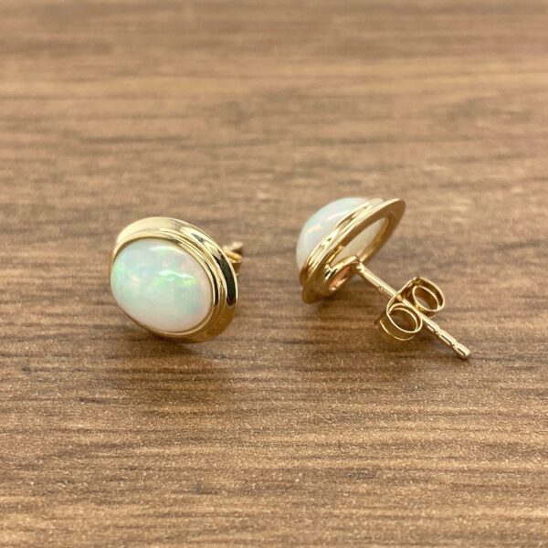 Gold opal stud earrings on wood.