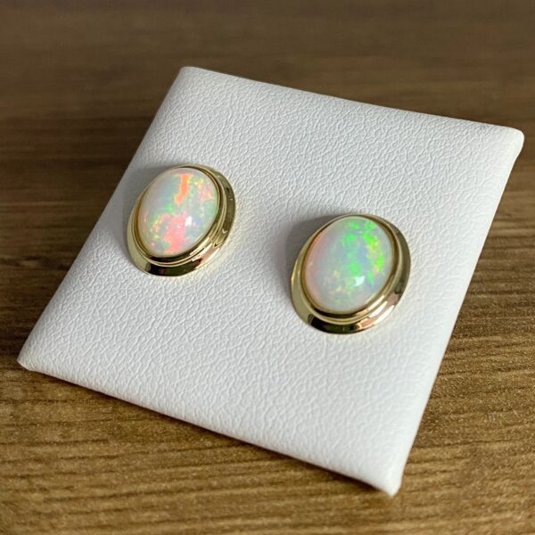 Gold opal earrings on white display.