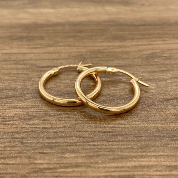 Two gold hoop earrings on a wooden table.