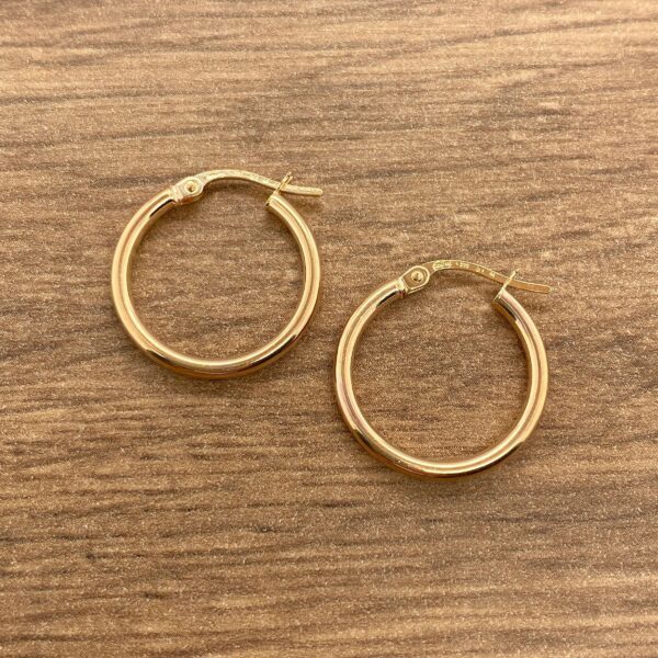 Gold hoop earrings on wooden background.