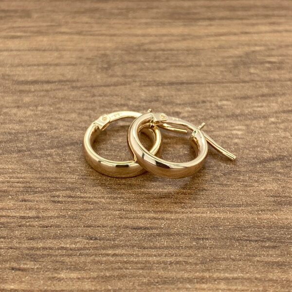 Gold hoop earrings on a wood surface.