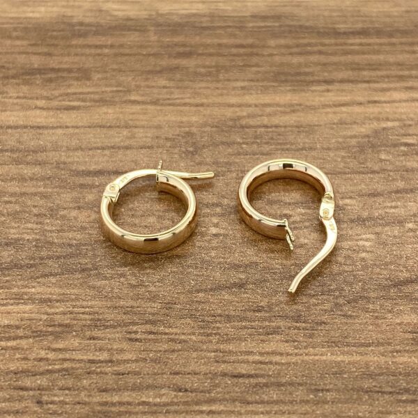 Gold hoop earrings on wooden surface.