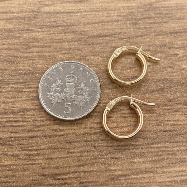 Gold hoop earrings next to a coin.